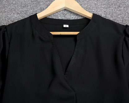 Camicia nera elegante su gruccia di legno, tessuto morbido, scollo a V, sfondo grigio. Abbigliamento moda donna, taglia media.