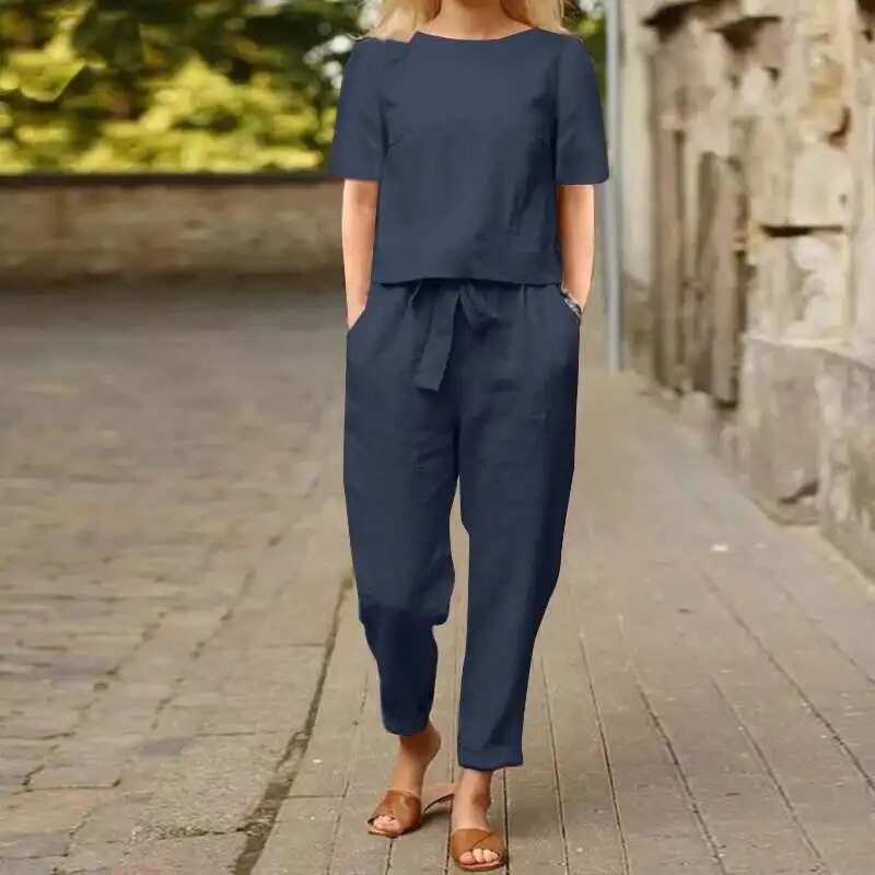 Donna con tuta blu scuro in lino, maniche corte, pantaloni larghi, sandali marroni, cammina su strada lastricata. Moda estiva casual elegante.