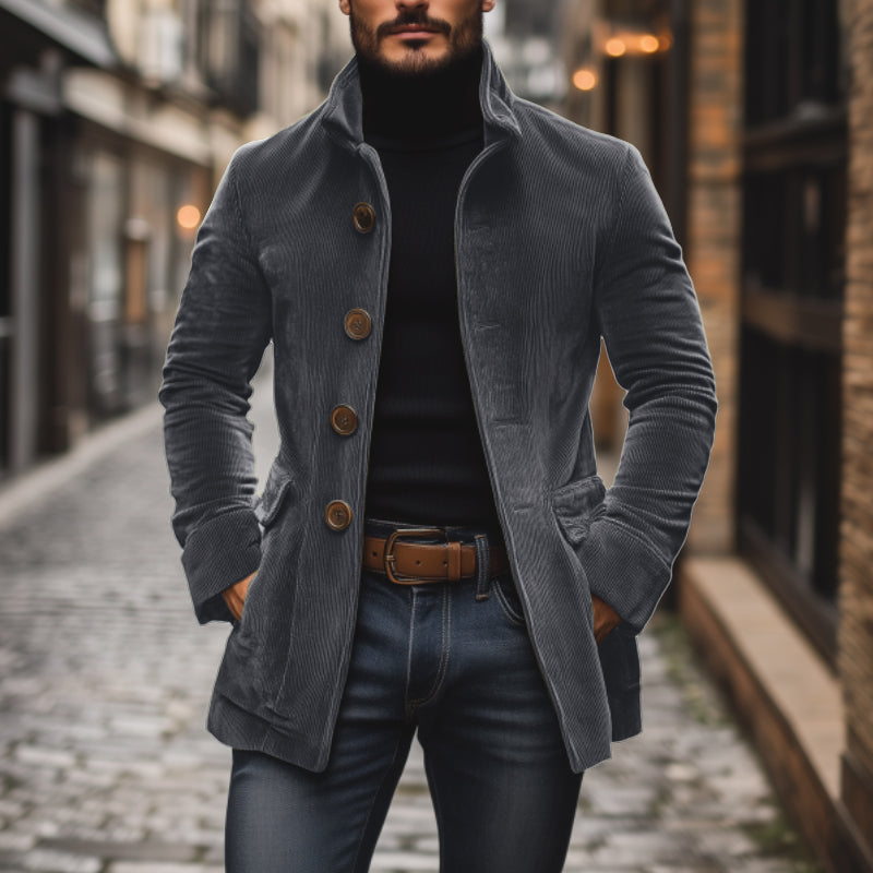 Uomo con cappotto di velluto a coste grigio, maglione nero e jeans, cammina su strada acciottolata. Moda maschile autunnale, stile urbano elegante.