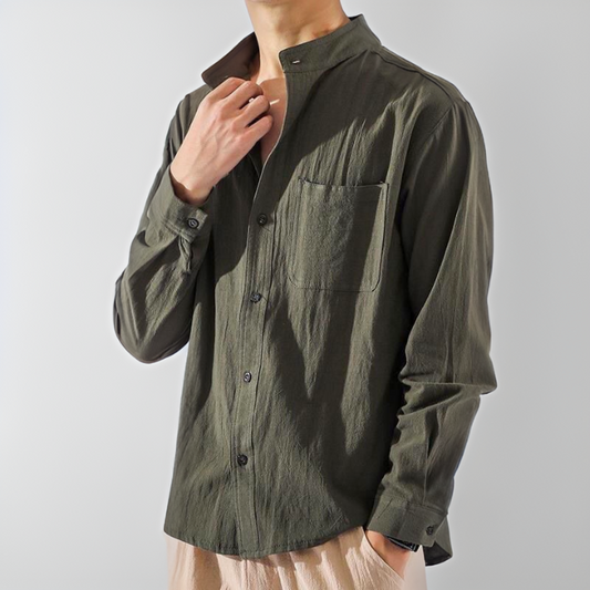 Camicia verde oliva da uomo con colletto alla coreana, taschino sul petto e bottoni neri, indossata con pantaloni beige. Moda casual maschile.