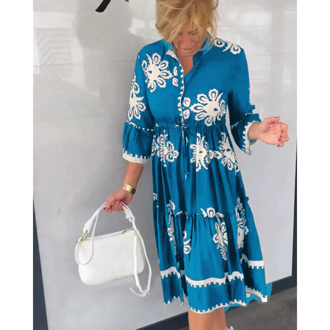 Donna con abito blu a fiori bianchi, maniche a tre quarti, tiene una borsa bianca. Moda estiva, abbigliamento casual elegante.