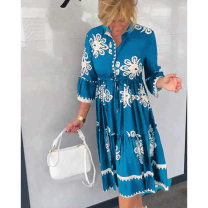 Donna con abito blu a fiori bianchi, maniche a tre quarti, tiene una borsa bianca. Moda estiva, abbigliamento casual elegante.