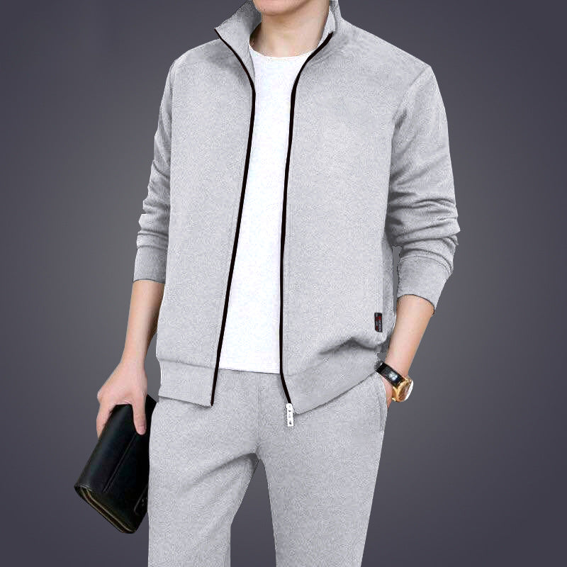 Uomo in tuta sportiva grigia, giacca con zip e pantaloni abbinati, tiene una borsa nera. Abbigliamento casual elegante, moda maschile.