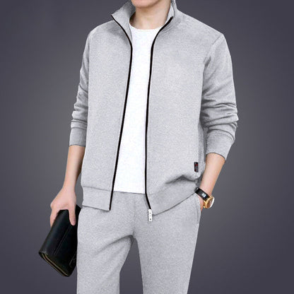 Uomo in tuta sportiva grigia, giacca con zip e pantaloni abbinati, tiene una borsa nera. Abbigliamento casual elegante, moda maschile.