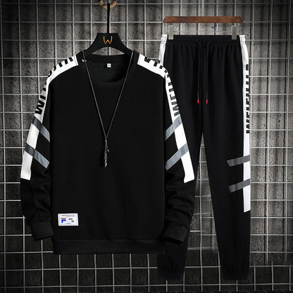 Completo sportivo nero da uomo, felpa e pantaloni con dettagli bianchi e grigi, appeso su griglia metallica. Stile casual, moda streetwear.