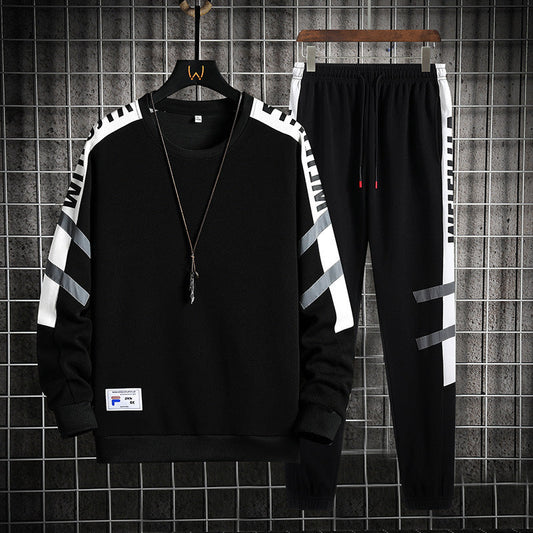 Completo sportivo nero da uomo, felpa e pantaloni con dettagli bianchi e grigi, appeso su griglia metallica. Stile casual, moda streetwear.