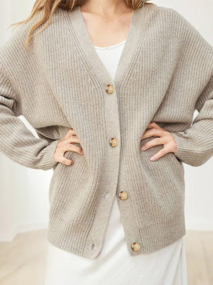 Donna indossa cardigan beige oversize in maglia con bottoni in legno, abbinato a vestito bianco. Moda autunnale, abbigliamento casual elegante.