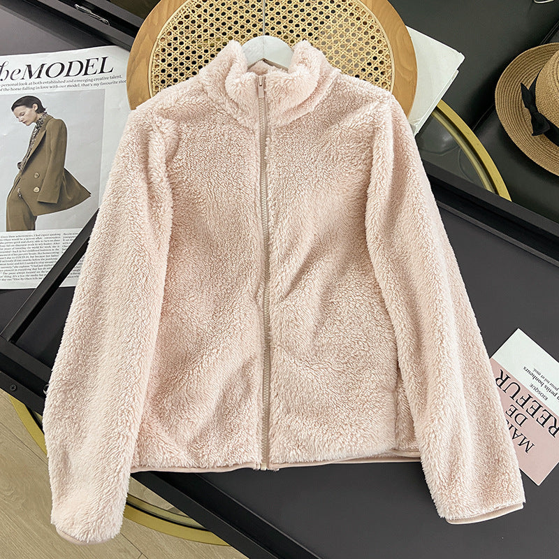 Giacca in pile rosa chiaro su tavolo nero, con zip frontale. Moda autunnale, abbigliamento caldo e morbido. Sfondo con rivista e cappello.