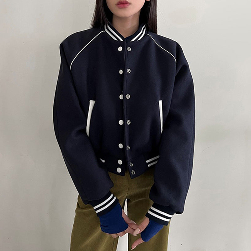 Giacca varsity blu scuro con bottoni bianchi, dettagli a righe su colletto e polsini, indossata da una persona. Stile casual e moderno.