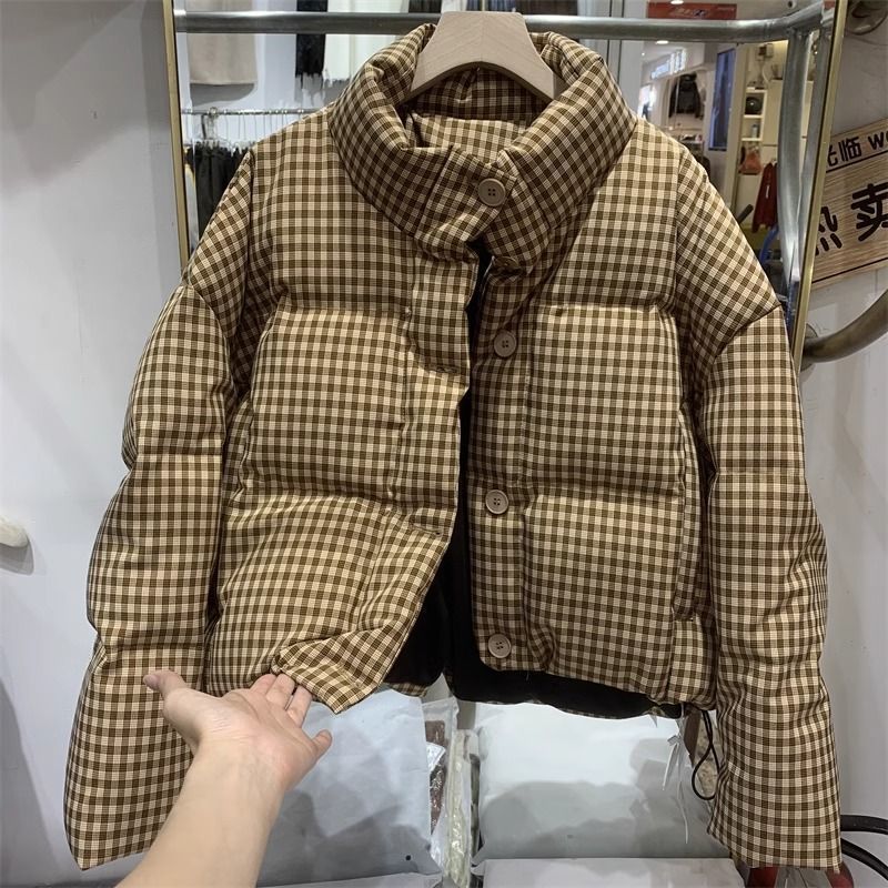 Giacca imbottita a quadri marroni e beige su appendiabiti, design invernale caldo, moda autunno inverno, abbigliamento casual elegante.