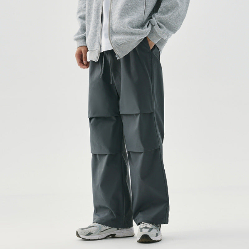 Pantaloni cargo grigi da uomo, design a strati, abbinati a felpa grigia e scarpe sportive bianche. Moda casual maschile, stile urbano.
