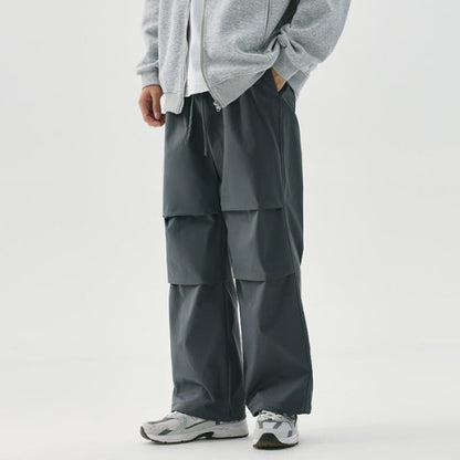 Pantaloni cargo grigi da uomo, design a strati, abbinati a felpa grigia e scarpe sportive bianche. Moda casual maschile, stile urbano.