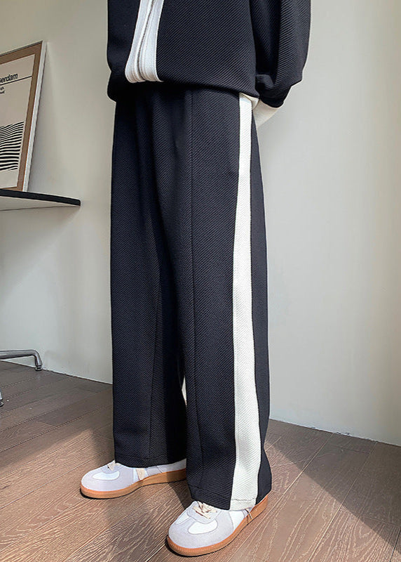 Pantaloni neri a gamba larga con striscia bianca laterale, abbinati a scarpe da ginnastica bianche. Stile casual moderno, moda uomo.