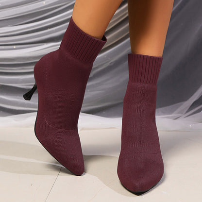Stivaletti a calza bordeaux con tacco a spillo, tessuto elasticizzato, su sfondo drappeggiato grigio. Scarpe moda donna eleganti e moderne.