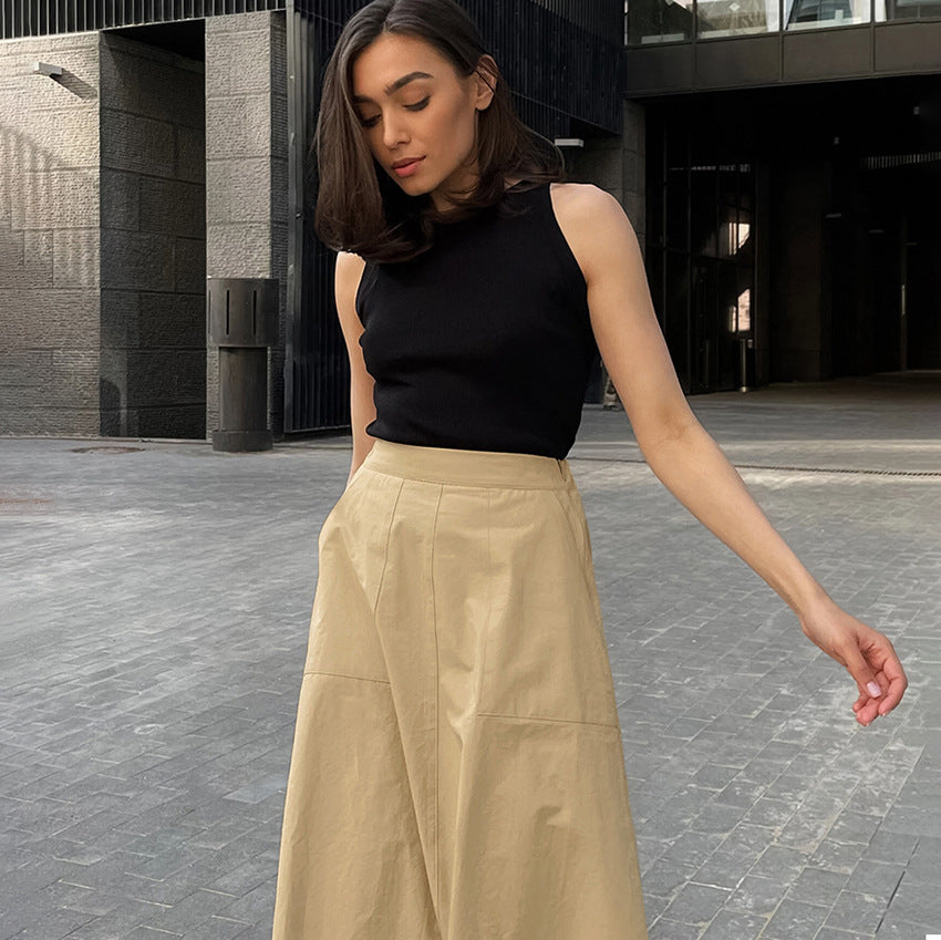 Donna con top nero e gonna beige in posa all'aperto, architettura moderna sullo sfondo. Moda urbana, abbigliamento casual chic, stile contemporaneo.