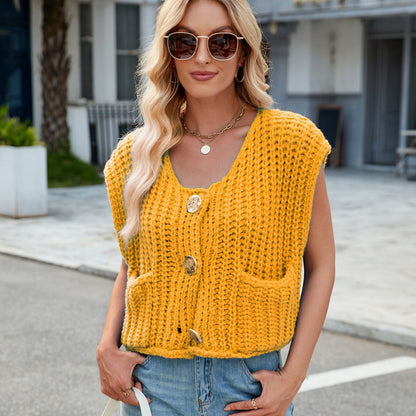 Donna con occhiali da sole indossa un gilet giallo lavorato a maglia con bottoni grandi e tasche, su strada urbana. Moda autunnale casual chic.