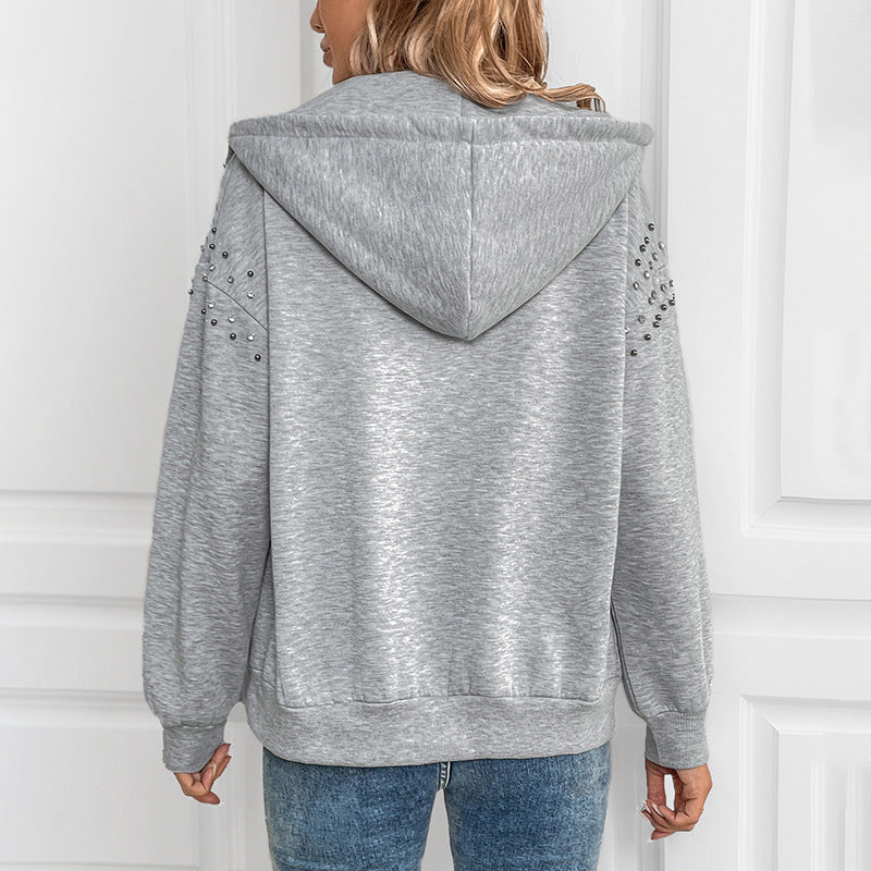 Donna con felpa grigia con cappuccio, decorata con borchie sulle maniche, vista posteriore. Abbigliamento casual, moda autunnale, stile urbano.