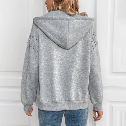 Donna con felpa grigia con cappuccio, decorata con borchie sulle maniche, vista posteriore. Abbigliamento casual, moda autunnale, stile urbano.