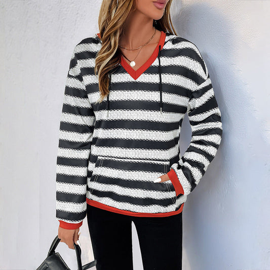 Donna con maglione a righe bianche e nere, bordi rossi, indossa collana e borsa nera. Moda casual autunnale, abbigliamento femminile trendy.