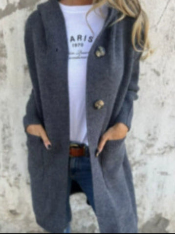 Donna con cappotto grigio lungo, bottoni grandi, tasche, indossa maglietta bianca con scritta "Paris", jeans blu. Moda autunnale casual.