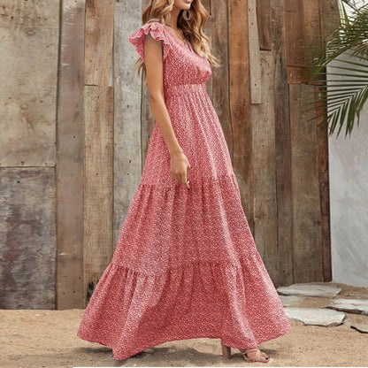 Donna in abito lungo floreale rosa, stile boho, posa davanti a parete di legno. Moda estiva, abbigliamento casual elegante, tendenze 2023.