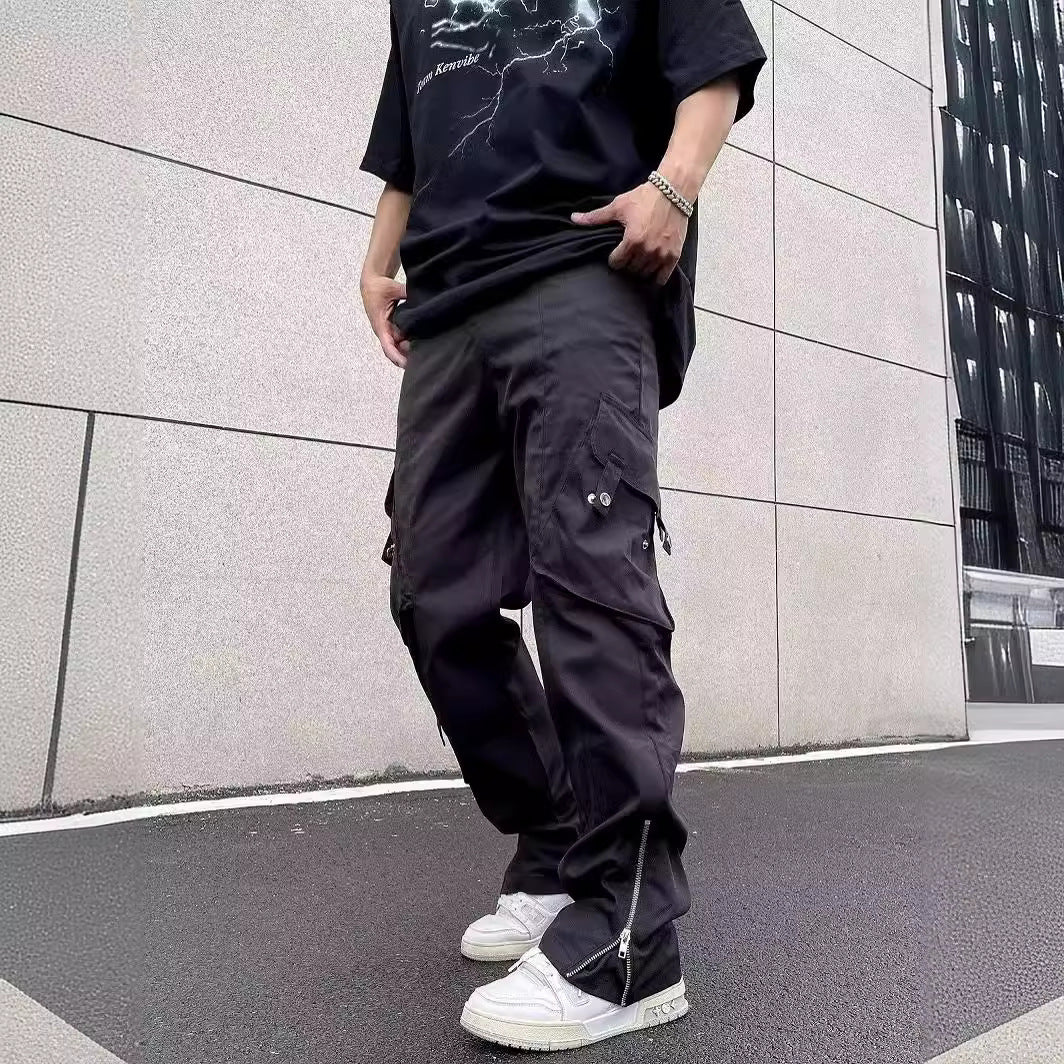 Uomo con pantaloni cargo neri e t-shirt nera, scarpe da ginnastica bianche, posa urbana su sfondo di edificio moderno. Moda streetwear casual.