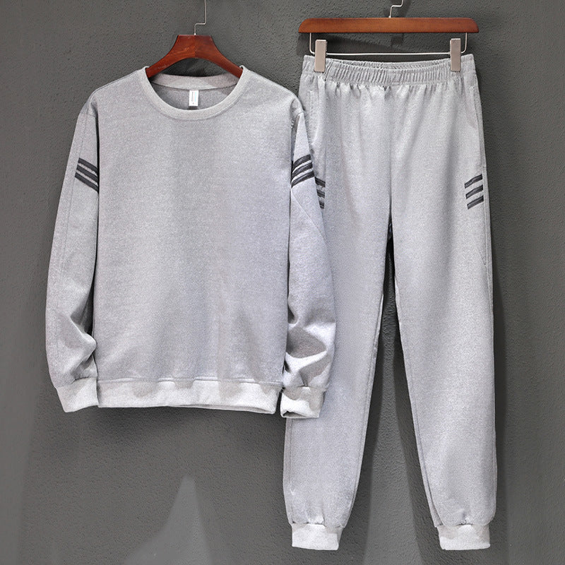 Tuta sportiva grigia in cotone, composta da felpa e pantaloni con dettagli a righe nere, appesa su grucce di legno. Abbigliamento casual uomo.