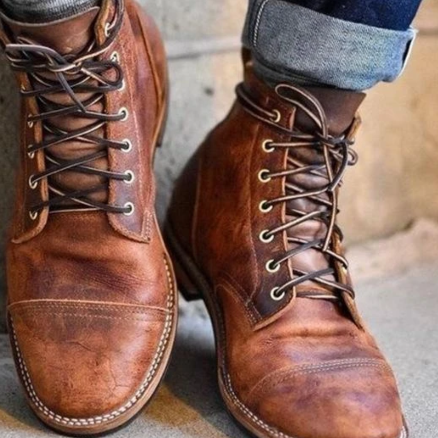 Stivali in pelle marrone da uomo, stile vintage, con lacci e cuciture a vista, indossati con jeans arrotolati. Moda maschile autunnale.