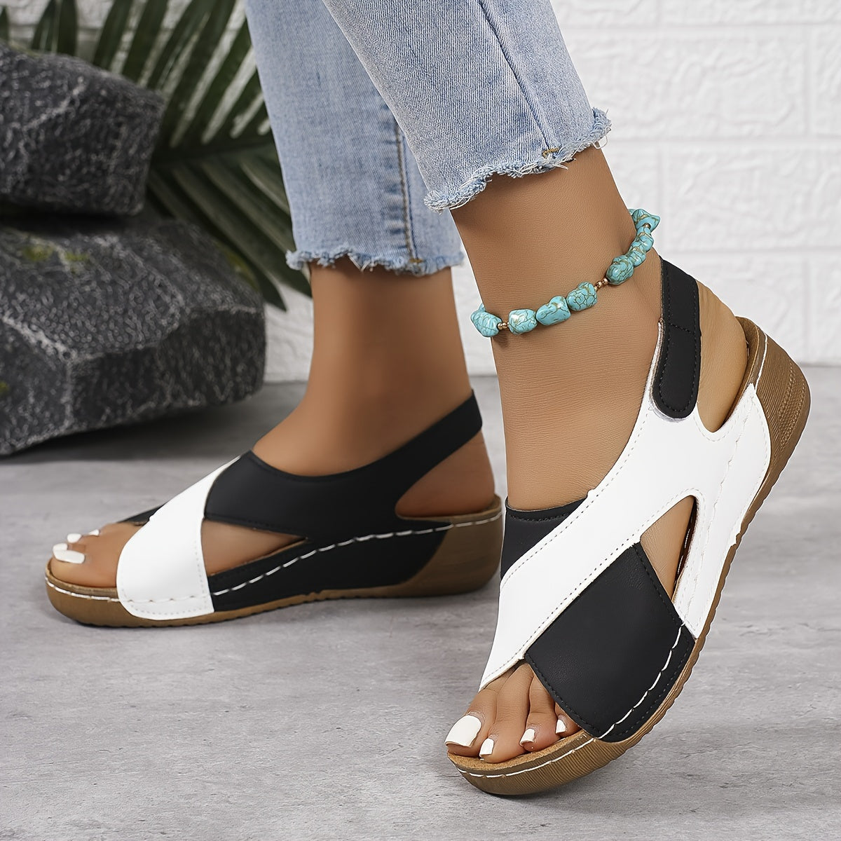 Sandali estivi donna bianchi e neri con zeppa, indossati con jeans chiari. Accessorio cavigliera turchese. Moda casual estiva.