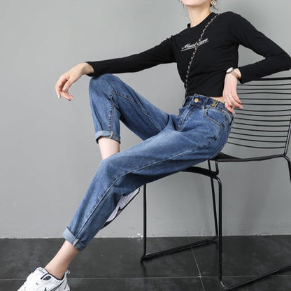 Donna seduta su sedia indossa jeans boyfriend e maglia nera a maniche lunghe. Look casual con scarpe da ginnastica bianche. Moda femminile moderna.