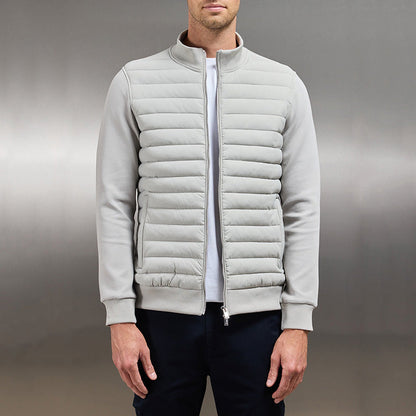 Giacca bomber uomo grigia, imbottita, con zip frontale, indossata su maglietta bianca e pantaloni scuri. Stile casual elegante.