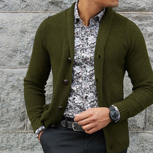 Uomo con cardigan verde oliva, camicia a fiori bianca e nera, orologio nero, pantaloni scuri. Moda maschile elegante e casual.