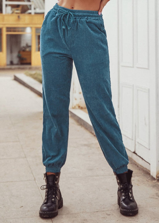 Pantaloni jogger in velluto a coste blu, indossati con stivali neri da donna. Moda casual autunnale, abbigliamento comodo e trendy.