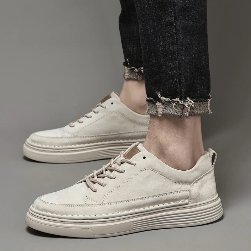 Scarpe da ginnastica beige su pavimento grigio, indossate con jeans neri strappati. Design moderno, suola spessa, stile casual.