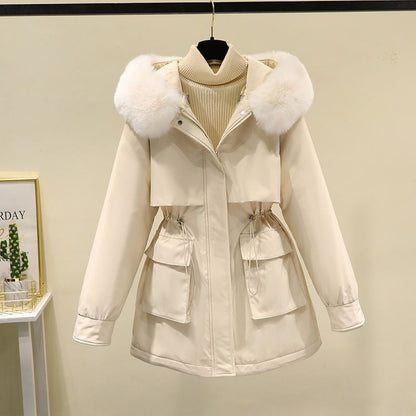 Giacca invernale beige con cappuccio in pelliccia bianca, tasche frontali e cintura regolabile, appesa su sfondo neutro. Moda donna, abbigliamento caldo.