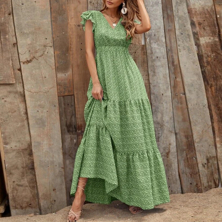 Donna con abito lungo verde a fiori, stile boho chic, posa davanti a parete di legno. Moda estiva, abbigliamento casual elegante.