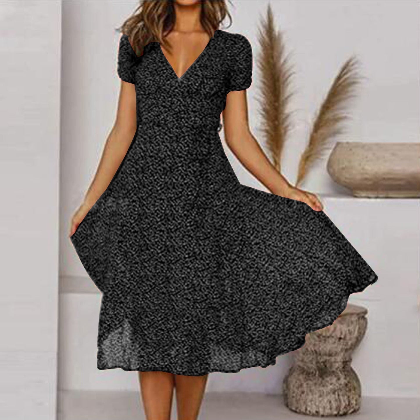 Abito nero a fiori con scollo a V e maniche corte, indossato da una donna in un ambiente moderno con decorazioni naturali. Moda femminile elegante.