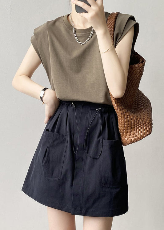Donna con maglietta marrone, gonna nera con tasche, borsa intrecciata marrone. Look casual chic, moda estiva, accessori minimalisti.