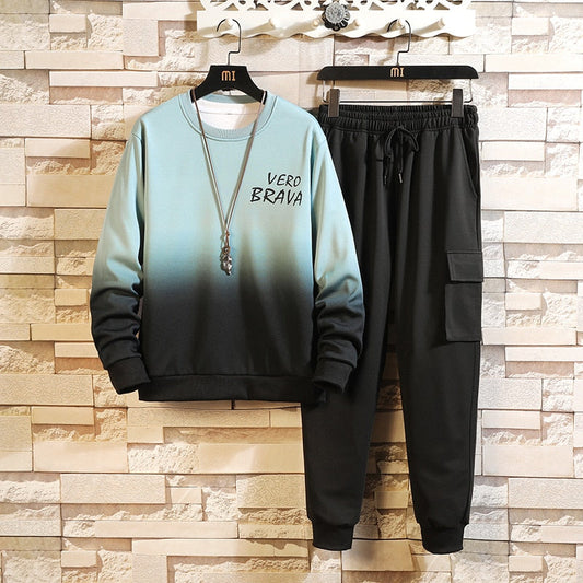 Tuta sportiva uomo, felpa sfumata blu-nero con scritta "Vero Brava", pantaloni neri cargo, appesa su sfondo muro mattoni.