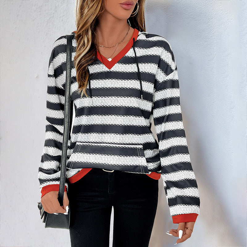 Donna con maglione a righe bianche e nere, dettagli rossi, borsa a tracolla nera. Moda casual autunnale, abbigliamento femminile trendy.
