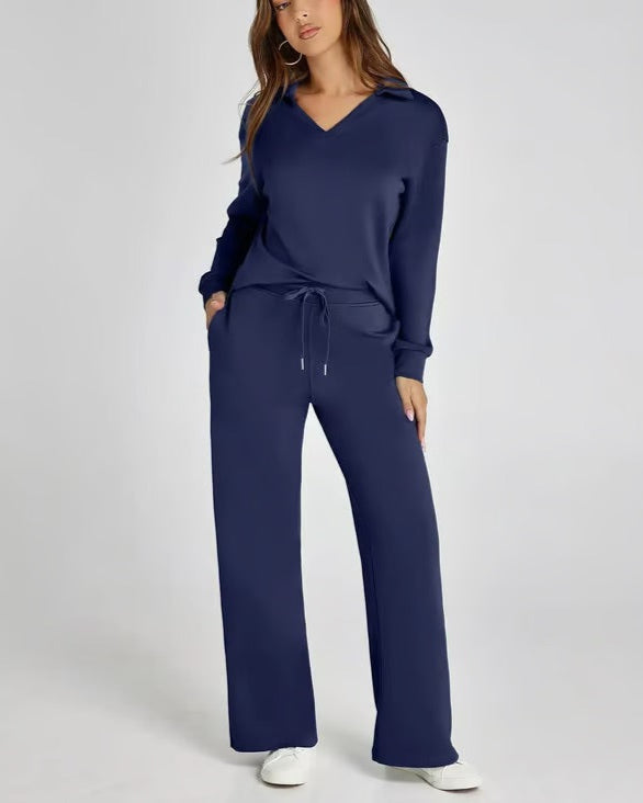 Donna in tuta blu scuro con cappuccio, pantaloni larghi e tasche, posa su sfondo bianco. Abbigliamento casual elegante, moda donna autunno.
