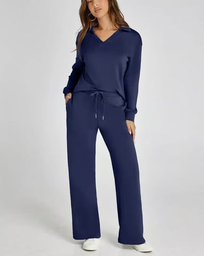 Donna in tuta blu scuro con cappuccio, pantaloni larghi e tasche, posa su sfondo bianco. Abbigliamento casual elegante, moda donna autunno.