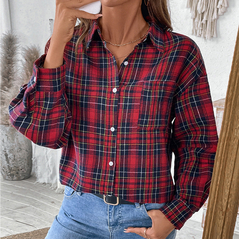 Donna con camicia a quadri rossa e blu, jeans casual, collana dorata, in ambiente moderno. Moda autunnale, stile casual chic.