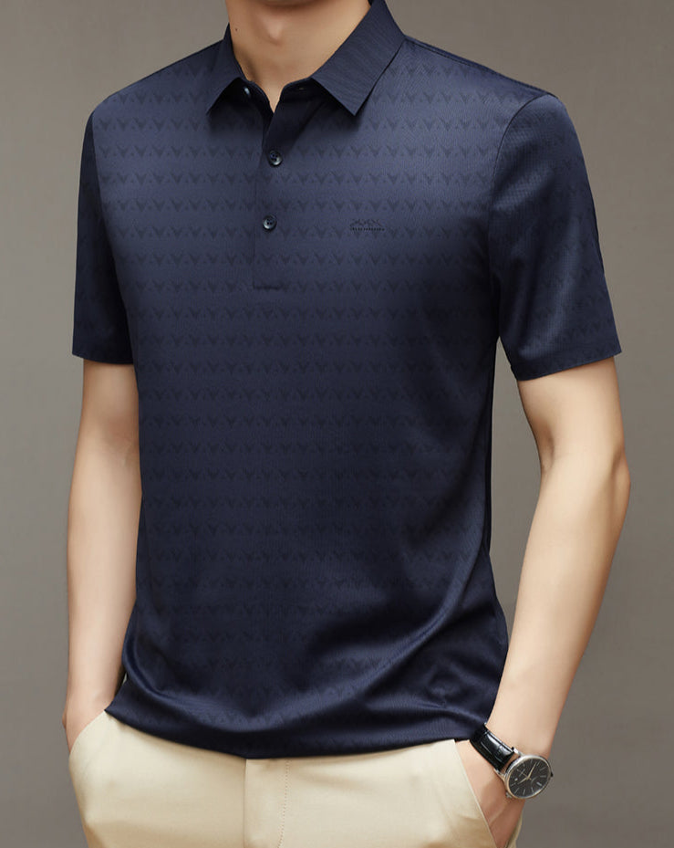 Uomo con polo blu scuro a maniche corte, motivo geometrico, indossa pantaloni beige e orologio nero. Elegante abbigliamento casual maschile.