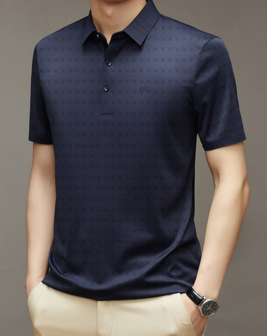 Uomo con polo blu scuro a maniche corte, motivo geometrico, indossa pantaloni beige e orologio nero. Elegante abbigliamento casual maschile.