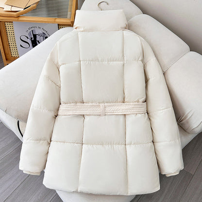 Giacca invernale bianca imbottita, design trapuntato, cintura in vita, su divano beige. Moda donna, abbigliamento caldo, stile casual chic.