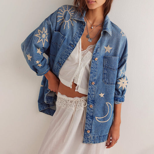 Giacca di jeans oversize con ricami di sole, luna e stelle, indossata sopra un top bianco e gonna lunga. Moda boho chic, abbigliamento casual.