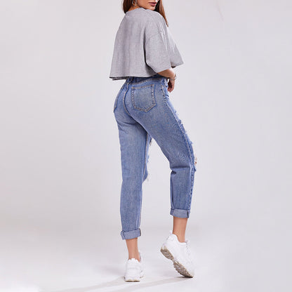 Donna in jeans strappati e maglietta grigia, scarpe da ginnastica bianche, posa di profilo. Moda casual, abbigliamento trendy, stile urbano.