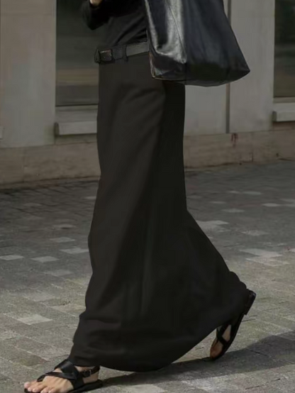 Uomo con gonna lunga nera, sandali e borsa in pelle nera, cammina su marciapiede. Moda maschile, abbigliamento unisex, stile urbano.