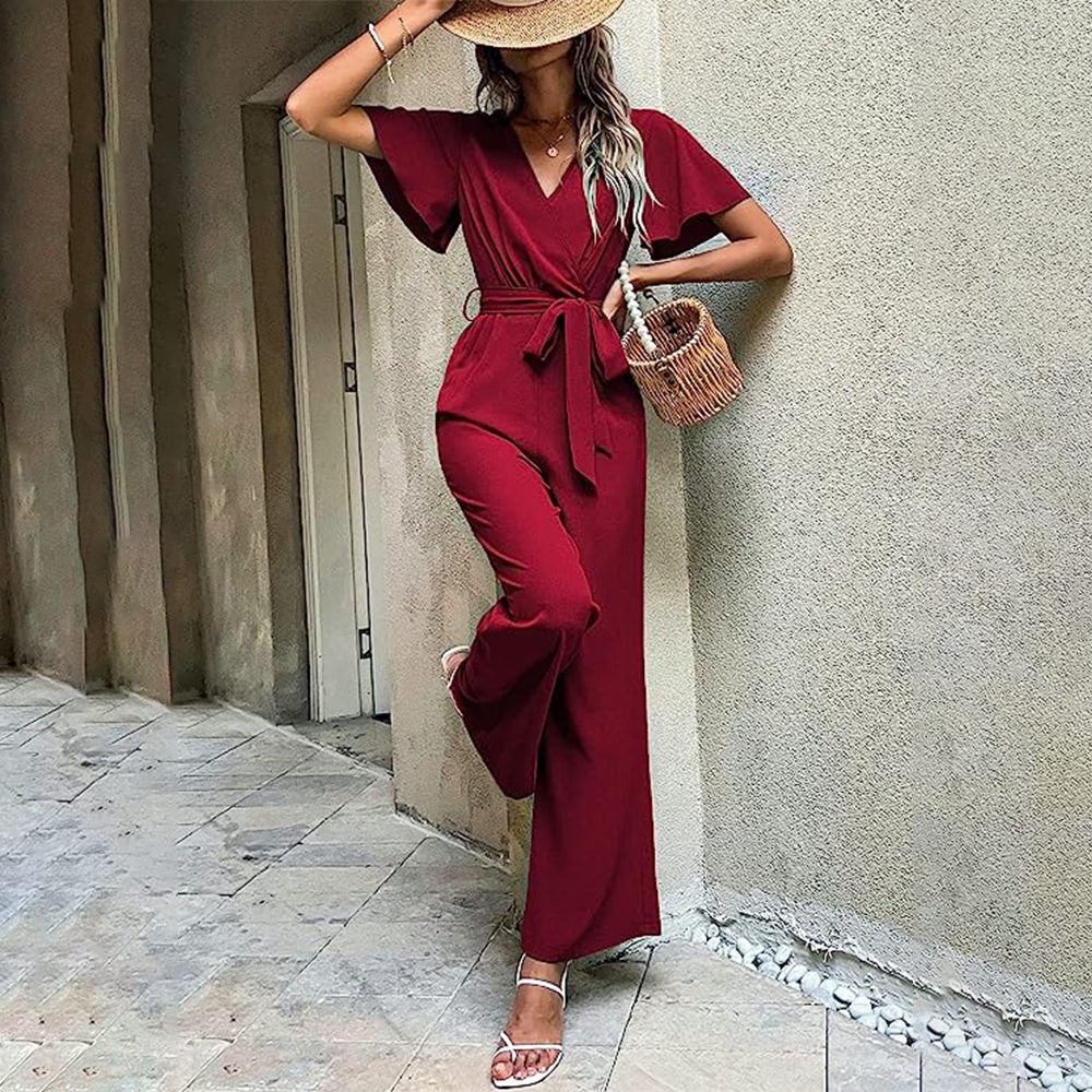 Donna in tuta rossa elegante, cappello di paglia, borsa intrecciata, sandali bianchi. Moda estiva, abbigliamento casual chic, stile urbano.